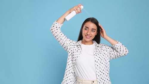 Young woman applying dry shampoo against light blue background
